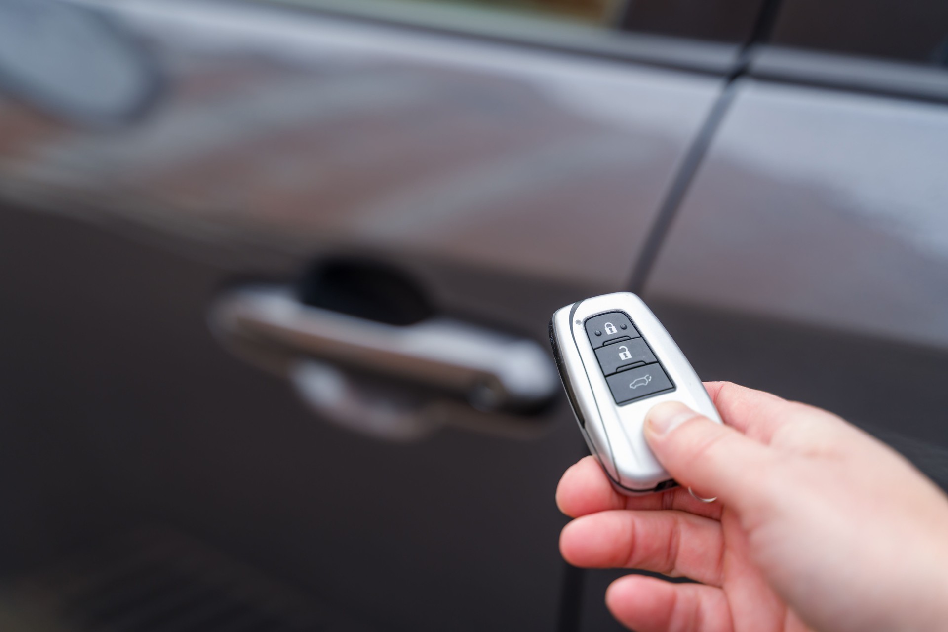 Hand holding car key remote control, unlocking vehicle